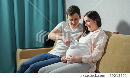 Father plays with baby on mother's belly with booties on hand Father plays with baby on mother's belly with booties on hand 89013521