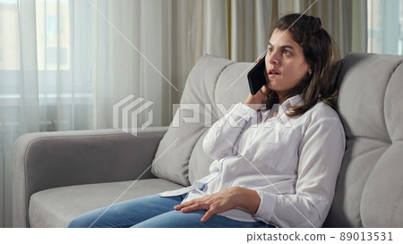 woman talks on mobile phone sitting on sofa at home woman talks on mobile phone sitting on sofa at home 89013531
