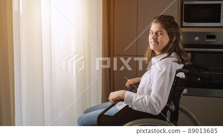 woman sits in wheelchair looking at camera at home woman sits in wheelchair looking at camera at home 89013685