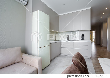 Modern beige and gray stylish kitchen with a table, soft chairs, a sofa and a beige refrigerator. Floor tiles and laminate. Built in household appliance 89015506