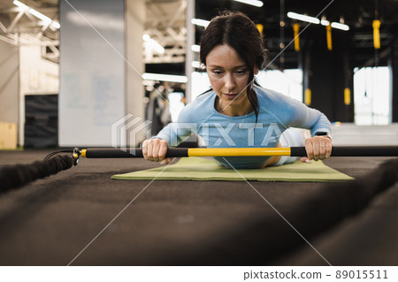 Sporty woman lies on the gym floor and does exercises with trx rip trainer 89015511