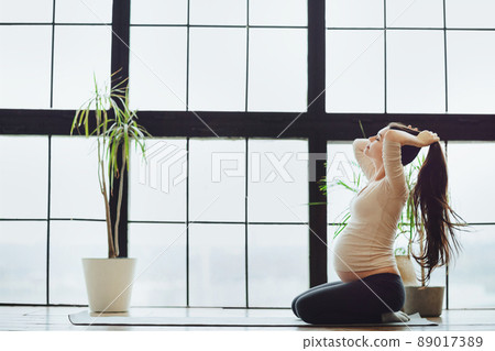 Sport and pregnancy. Young calm pregnant woman preparing for yoga or stretching practice at home 89017389