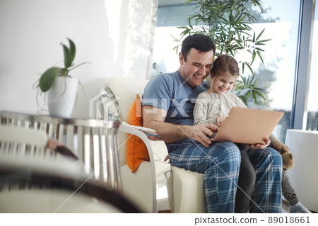 Happy young dad and preschooler daughter sit on couch watch cartoon on laptop together 89018661