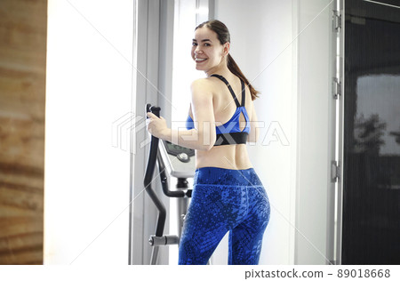 Smiling athletic woman dressed in a black sportswear running on the treadmill in the modern gym Smiling athletic woman dressed in a black sportswear running on the treadmill in the modern gym 89018668