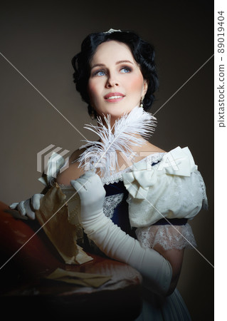 A lady with a smile in a historical costume with a feather in her hand and a letter. Design for the cover of the book. Fashion of 19th century, dress with crinoline of 1860. High quality photo A lady with a smile in a historical costume with a feather in her hand and a letter. Design for the cover of the book. Fashion of 19th century, dress with crinoline of 1860. High quality photo 89019404