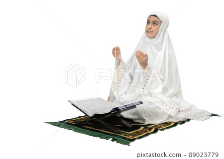 Asian Muslim woman in a veil sitting while raised hands and praying with prayer beads Asian Muslim woman in a veil sitting while raised hands and praying with prayer beads 89023779