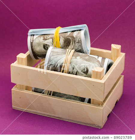 Paper dollars wrapped with an elastic band in a wooden box on a red background 89023789