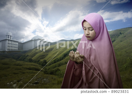 Asian Muslim woman in a veil standing while raised hands and praying 89023831