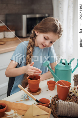 Little girl sitting at the table at home, sowing seeds into flower pots. 89024468