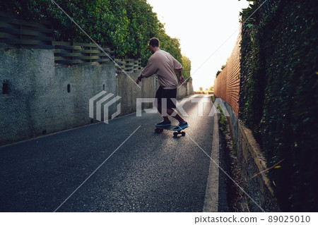 Rear view of skilled male skater practice freestyle on board on rural asphalt road during leisure time 89025010