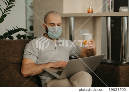 A man in a face mask working remotely on his laptop during the quarantine. 89025703