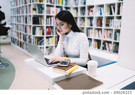 Thoughtful elegant ethnic lady working at laptop in library 89026325