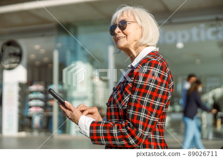 Smiling senior woman wearing sunglasses standing in city Smiling senior woman wearing sunglasses standing in city 89026711