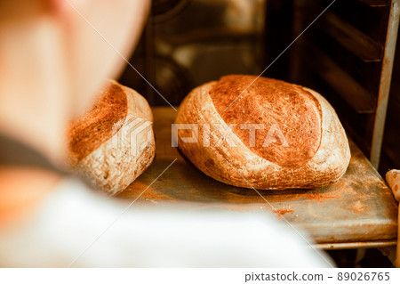 Baker takes tray with breads out of oven in modern workshop closeup 89026765