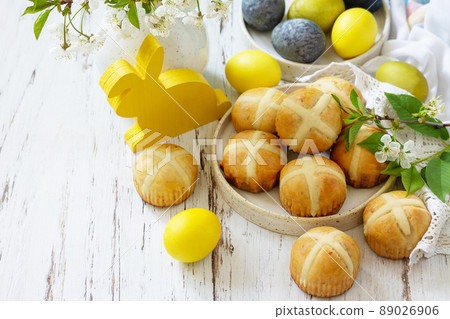 Happy Easter festive food concept. Homemade Easter traditional hot cross buns with raisin and natural colorful easter eggs on a rustic table. Copy space. 89026906