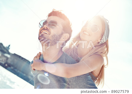 Outdoors photo of happy boyfriends piggybacking their girlfriends at sunset on beach 89027579