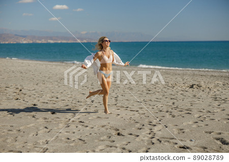 Excited slim lady running along the beach on a sunny summer day 89028789