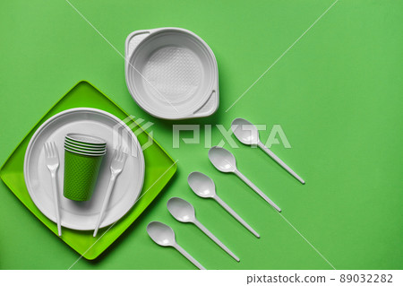 Colorful plastic disposable tableware on green background with copy space. The concept of picnic utensil. Top view. Selective focus. Close-up. 89032282
