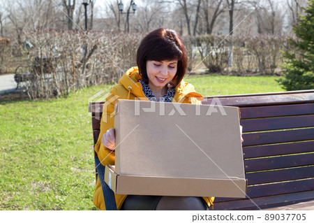 A happy woman with a smile opens a box with a new laptop on the street 89037705