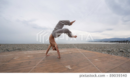 Shirtless caucasian man doing backflip on pebble beach. Shirtless caucasian man doing backflip on pebble beach. 89039340