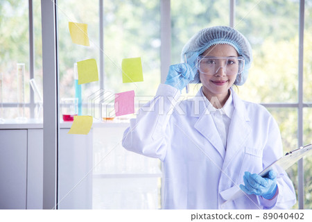 Woman scientist hand write note information in medical lab look at science microscope medical test, research biology chemistry. Asian Females technician laboratory analyzing blood test pharmaceutical 89040402