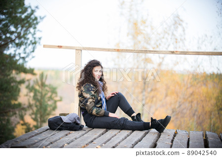 Young woman sitting on a platform on a background of the forest, daylight Young woman sitting on a platform on a background of the forest, daylight 89042540