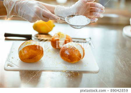 Confectioner pours powdered sugar onto delicious buns with cream in craft bakery Confectioner pours powdered sugar onto delicious buns with cream in craft bakery 89042859