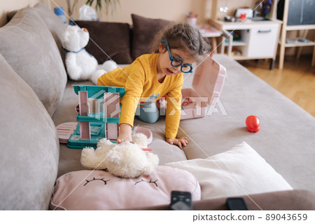 Adorable little girl playing doctor in her room. Cute three year old girl spend time playing. Girls wearing glasses yellow blouse and blue leggings. Ukrainian cute kid. Background of her kids kitchen Adorable little girl playing doctor in her room. Cute three year old girl spend time playing. Girls wearing glasses yellow blouse and blue leggings. Ukrainian cute kid. Background of her kids kitchen 89043659