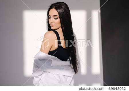 Pretty brunette hair woman in blue jeans and white shirt standing in front of white wall. Shadow on white background Pretty brunette hair woman in blue jeans and white shirt standing in front of white wall. Shadow on white background 89048032