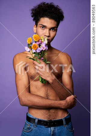 Handsome young transgender model with flowers in hand standing on purple background. Glamour fashion 89049563