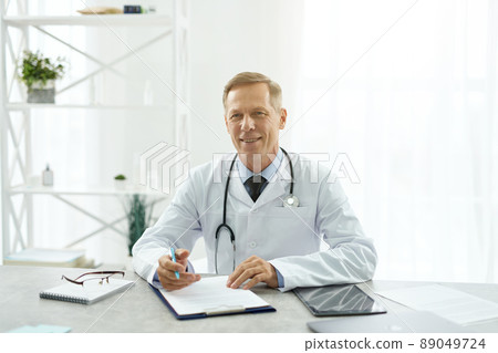 Cheerful male doctor sitting at the table in clinic 89049724