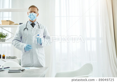 Male doctor in medical mask holding test tube Male doctor in medical mask holding test tube 89049725