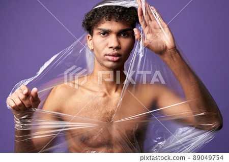 Young transgender man with destroy plastic bag on nude muscular body. Trans gender male can breathe Young transgender man with destroy plastic bag on nude muscular body. Trans gender male can breathe 89049754