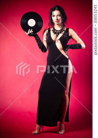 Vintage photo of a glamorous pinup girl, holding a vinyl record and looking up on a pink background. 89053245