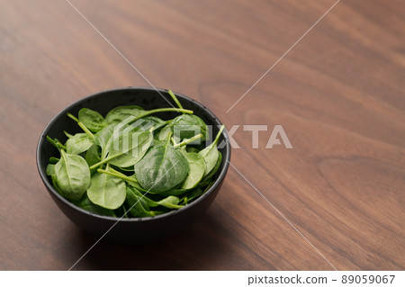 Fresh spinach leaves in black bowl on walnut wood table Fresh spinach leaves in black bowl on walnut wood table 89059067