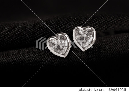 Hearts-shaped silver stud earrings on black fabric background. Hearts-shaped silver stud earrings on black fabric background. 89061936