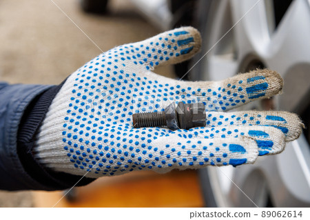 mechanic hand in fabric glove holding car wheel bolt 89062614
