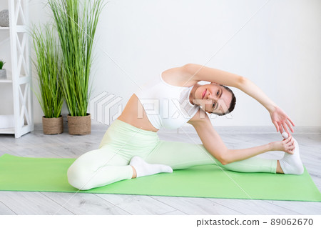 Yoga practice. Home training. Healthy lifestyle. Active people. Sporty flexible woman in activewear doing stretch exercise on mat at light apartment interior. Yoga practice. Home training. Healthy lifestyle. Active people. Sporty flexible woman in activewear doing stretch exercise on mat at light apartment interior. 89062670