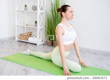 Gymnastics workout. Indoor training. Healthy wellbeing. Calm sportive young fit woman in activewear praciticing flexibility exercise on yoga mat at home gym. Gymnastics workout. Indoor training. Healthy wellbeing. Calm sportive young fit woman in activewear praciticing flexibility exercise on yoga mat at home gym. 89062671