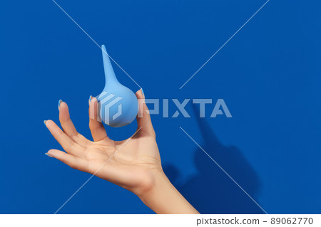 Wellgroomed womans hand holding enema on blue background Wellgroomed womans hand holding enema on blue background 89062770