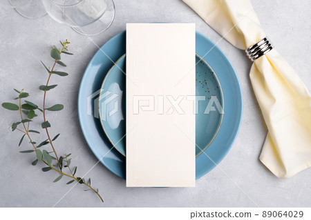 Menu card mockup on blue plate with festive wedding or birthday table setting with eucalyptus branch on grey background Menu card mockup on blue plate with festive wedding or birthday table setting with eucalyptus branch on grey background 89064029