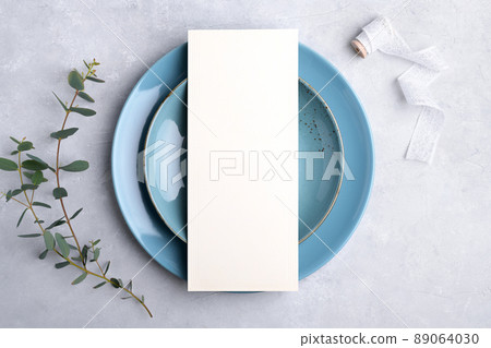 Menu card mockup on blue plate with festive wedding or birthday table setting with eucalyptus branch on grey background 89064030
