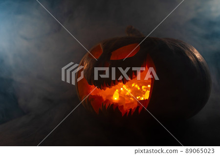 A creepy pumpkin with a carved grimace in the smoke. Jack o lantern in the dark. 89065023