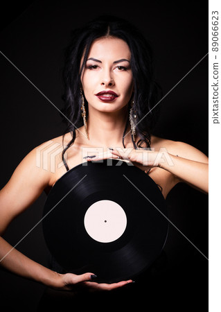 Vintage photo of a glamorous pinup girl, holding a vinyl record and looking up on a pink background. Vintage photo of a glamorous pinup girl, holding a vinyl record and looking up on a pink background. 89066623