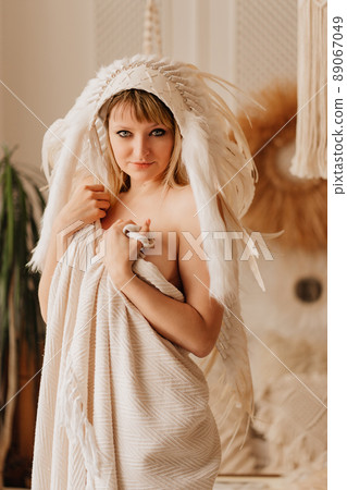 a beautiful blonde woman in a blanket in an Indian headdress of white feathers a beautiful blonde woman in a blanket in an Indian headdress of white feathers 89067049