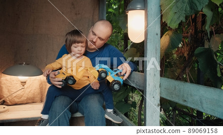 Father with a small child is sitting on the porch of an old house and playing with his cute baby in toy car. The concept of family pastime and the relationship between children and parents Father with a small child is sitting on the porch of an old house and playing with his cute baby in toy car. The concept of family pastime and the relationship between children and parents 89069158