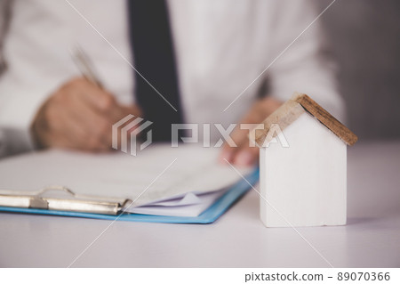Hands of business man sign agreement buying home while model home on desk. Hands of business man sign agreement buying home while model home on desk. 89070366