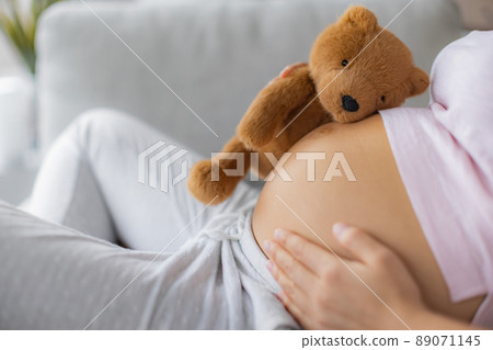 Pregnant woman caressing belly hugging teddy bear baby toy on pregnancy bump waiting for the birth of her child Pregnant woman caressing belly hugging teddy bear baby toy on pregnancy bump waiting for the birth of her child 89071145