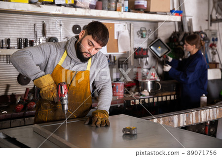 Confident man mechanic drilling metal sheet in workshop Confident man mechanic drilling metal sheet in workshop 89071756