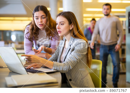 Two women friends studying together at library Two women friends studying together at library 89071767